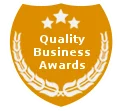 A golden shield-shaped emblem featuring three stars and the text 'Quality Business Awards' surrounded by laurel leaves.