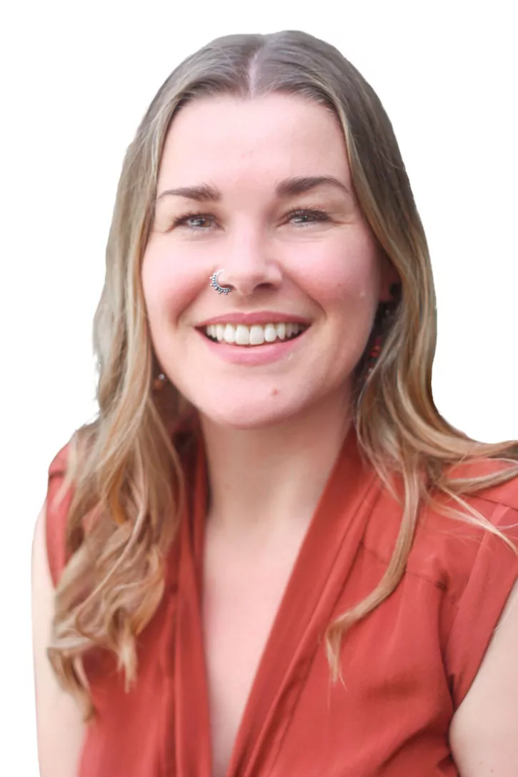A smiling woman with long, wavy hair, wearing an orange top and earrings, with a joyful expression against a white background.