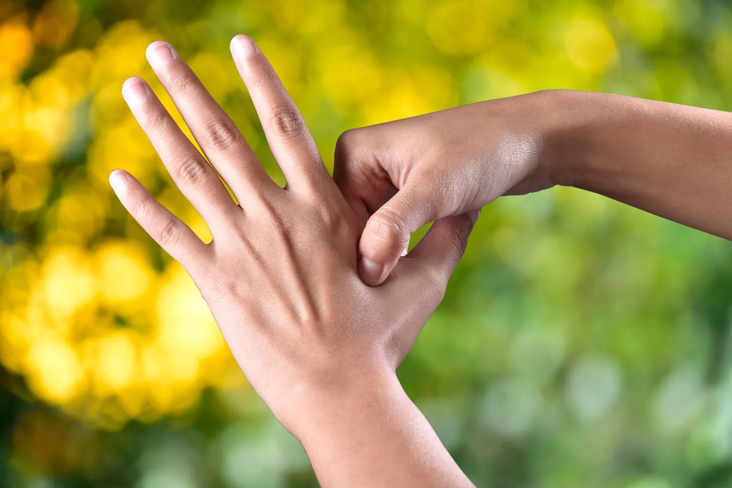 A close-up of a hand performing a wrist stretch against a blurred natural background.